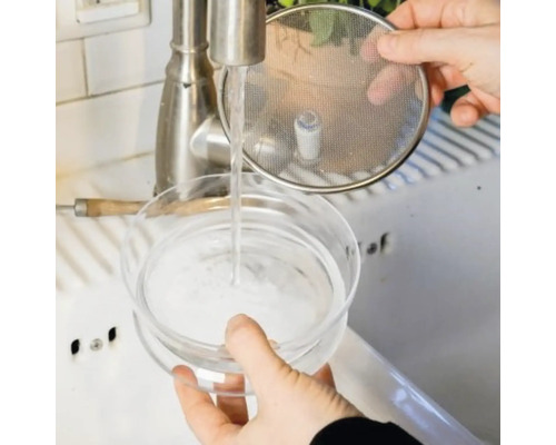 Une personne lave une cafetière à infusion froide sous un robinet.