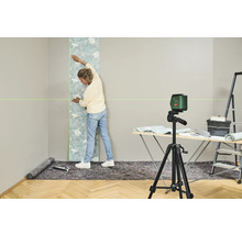 Une femme pose du papier peint sur un mur à l'aide d'un niveau laser