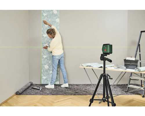 Une femme pose du papier peint sur un mur à l'aide d'un niveau laser