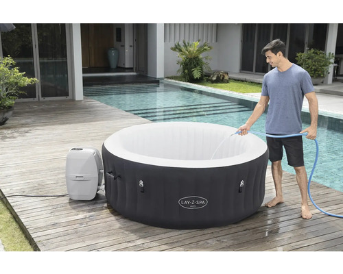 Jacuzzi Lay-Z-Spa gonflable avec un homme le remplissant avec un tuyau, sur une terrasse en bois