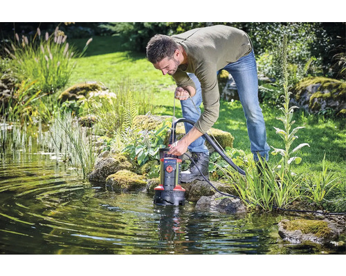 Mann bedient eine Teichpumpe im Gartenteich.