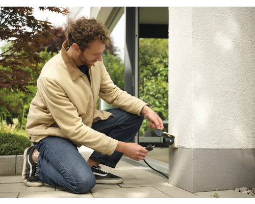 Mann schliesst Aussensteckdose an Hauswand an