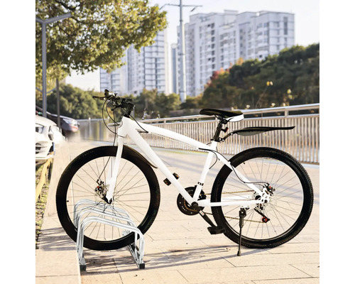 Vélo blanc garé sur un range-vélos devant un paysage urbain.