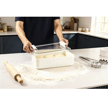 Szene in einer Küche: Ein Mann öffnet eine Frischhaltebox mit Teiglingen, umgeben von Mehl, einem Nudelholz und Ausstechformen.