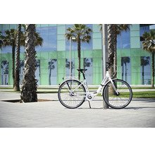 Vélo de ville blanc appuyé contre un poteau devant des palmiers et un bâtiment.