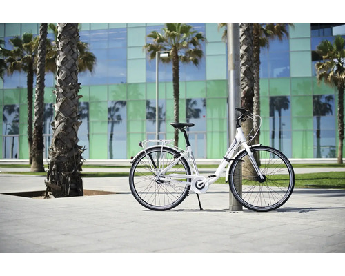 Vélo de ville blanc appuyé contre un poteau devant des palmiers et un bâtiment.