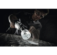 Un homme perce un trou dans une surface métallique avec une scie cloche.