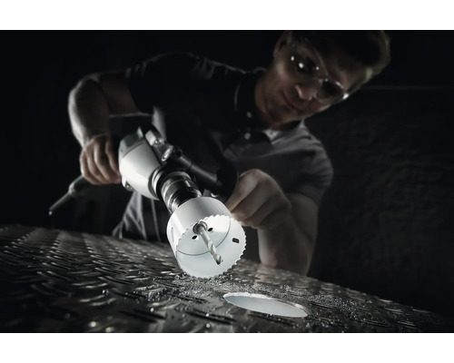 Un homme perce un trou dans une surface métallique avec une scie cloche.