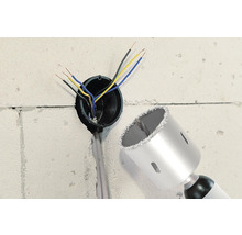 Wand mit Bohrloch, Elektrokabeln und einer Bohrkrone.