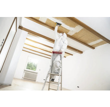 Artisan sur une échelle effectuant des travaux de rénovation sur un plafond dans une pièce lumineuse.