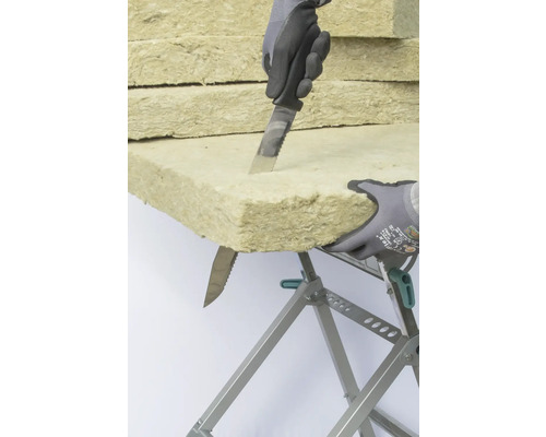 Dämmstoff wird mit einem Messer auf einer Werkbank zugeschnitten.