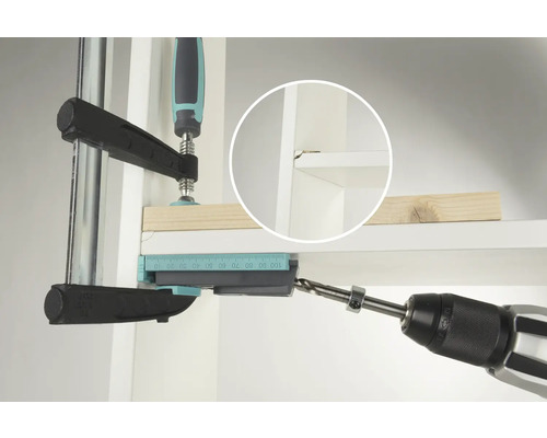 Eine Bohrmaschine bohrt ein Loch mit Hilfe einer Bohrlehre in ein Regal.