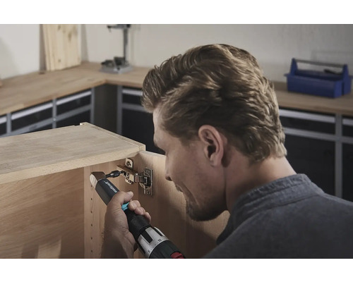 Ein Mann befestigt ein Scharnier mit einem Akku-Bohrschrauber an einem Holzschrank.