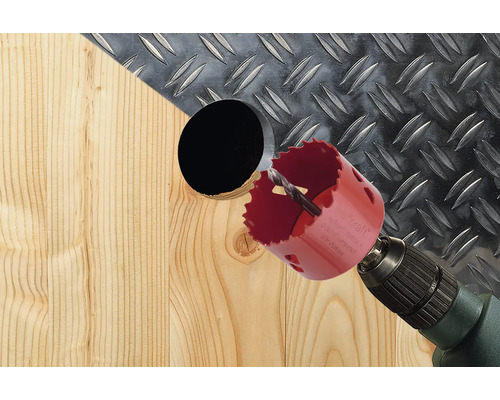 Lochsäge bohrt Loch in Holz mit Riffelblech im Hintergrund