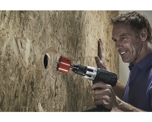 Mann bohrt Loch mit Lochsäge in Holzplatte