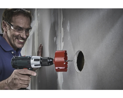 Mann bohrt mit einer Lochsäge ein Loch in eine Wand.