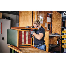 Un homme fixe le ressort d'un fauteuil avec un cloueur à air comprimé.