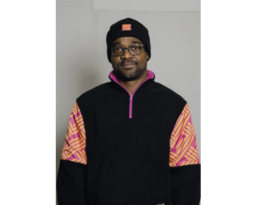 Un homme portant des lunettes et un bonnet porte un haut en polaire noir avec des manches colorées.