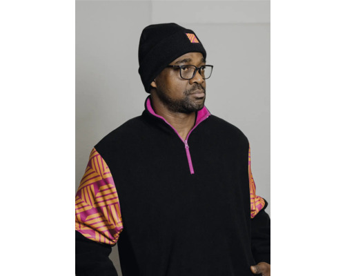 Homme avec des lunettes et un bonnet, portant un pull avec une fermeture éclair