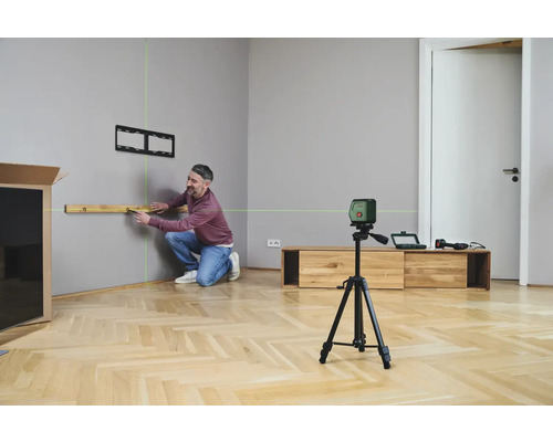 Un homme utilise un niveau laser pour aligner une étagère sur un mur