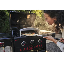 Frau schiebt Pizza mit Pizzaschieber in Gasgrill mit Pizzaofenaufsatz