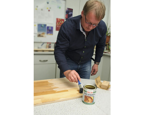 Un homme applique du vernis pour bateaux et yachts sur une planche de bois