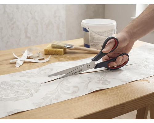 Une personne coupant un morceau de papier peint à motifs avec des ciseaux Rautner sur une table