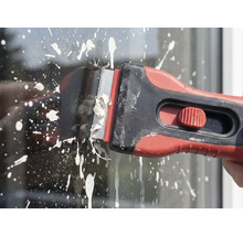 Farbschaber in Gebrauch zum Entfernen von Farbspritzern auf Glas.