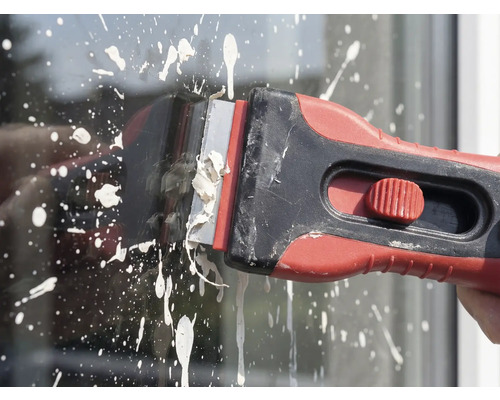 Farbschaber in Gebrauch zum Entfernen von Farbspritzern auf Glas.