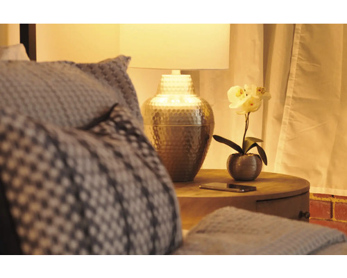Nachttisch mit Lampe, Dekoration und Textilien in einem Schlafzimmer