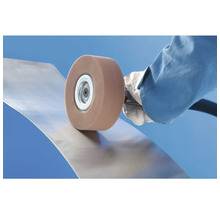 Utilisation d'une meule abrasive rotative pour le traitement de surface d'une tôle métallique courbée.