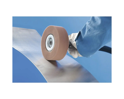 Utilisation d'une meule abrasive rotative pour le traitement de surface d'une tôle métallique courbée.