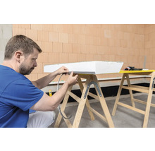 Mann befestigt Dichtband an einer Dämmplatte auf einer Werkbank.