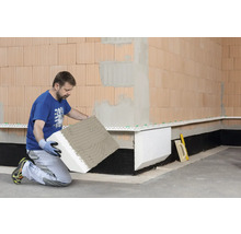 Mann befestigt Perimeterdämmplatten an einer Hauswand.