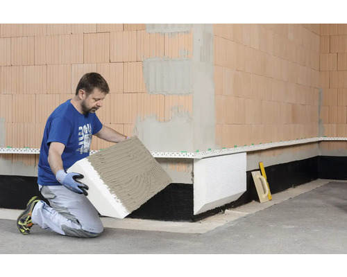 Handwerker bringt Perimeterdämmung an einer Wand an.
