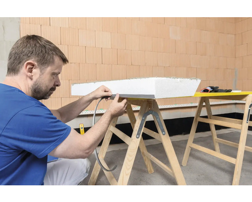 Mann befestigt Dichtungsband an einer Dämmplatte auf einer Arbeitsbock-Konstruktion.