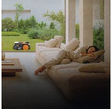 Frau entspannt auf der Couch, während ein Rasenmähroboter den Rasen mäht