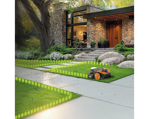 Ein Rasenmähroboter mäht den Rasen vor einem Wohnhaus mit Steinfassade.