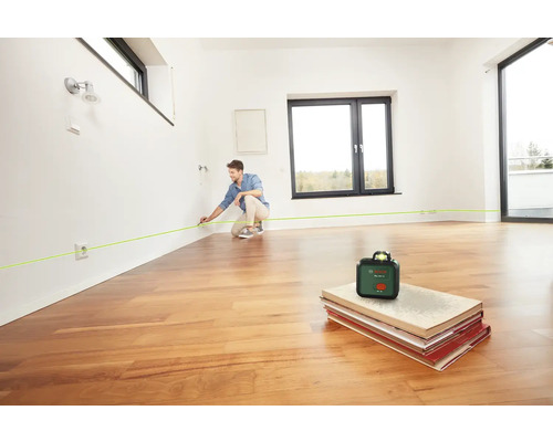 Mann benutzt Bosch PLL 360 Kreuzlinienlaser in einem Raum mit Holzboden.