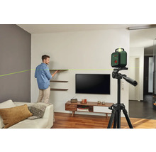 Mann montiert Regale mit einem Bosch Kreuzlinienlaser auf einem Stativ in einem Wohnzimmer