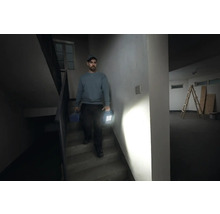 Un homme descend un escalier avec une boîte à outils et une lampe de travail à la main