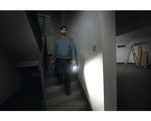 Un homme descend un escalier avec une boîte à outils et une lampe de travail à la main
