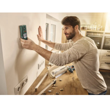 Un homme utilise un détecteur sur un mur dans une pièce pour préparer des travaux d'installation.