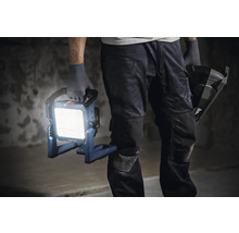 Un artisan tient une lampe de chantier Bosch allumée à la main.