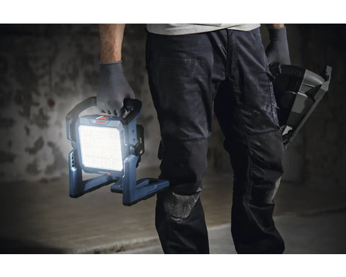 Un artisan tient une lampe de chantier Bosch allumée à la main.