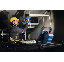 Un artisan avec casque de protection et harnais de sécurité travaille avec une scie sauteuse à la lumière d'un projecteur.