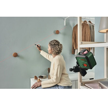 Une femme utilise un niveau laser pour marquer une ligne sur un mur pour fixer des crochets muraux.