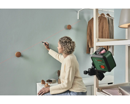 Une femme utilise un niveau laser pour marquer une ligne sur un mur pour fixer des crochets muraux.