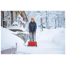 Femme utilisant un épandeur pour l'entretien hivernal sur un trottoir enneigé.