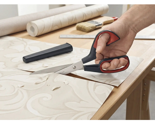 Des ciseaux à papier peint coupent du papier peint sur une table.